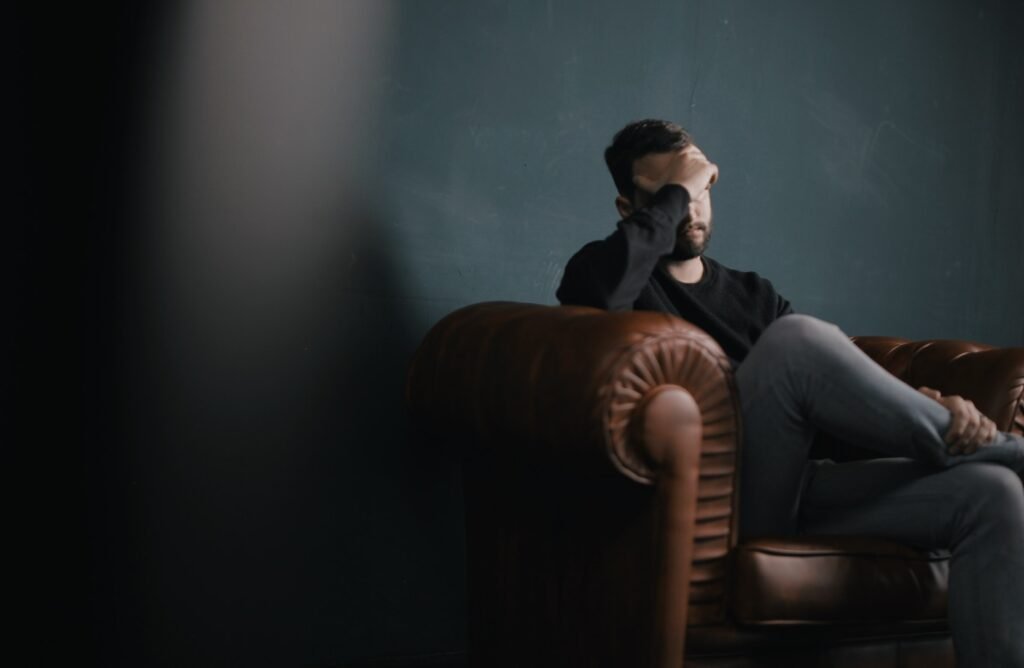 Stressed man sitting on a leather couch with his hand on his forehead