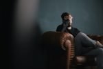 Stressed man sitting on a leather couch with his hand on his forehead
